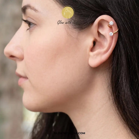 12mm Stainless Steel Helix Piercing Jewelry Ear Jewlery - 12mm Stainless Steel Helix Piercing Jewelry Ear JewleryJewelryGlow With NazGlow With NazE049A close-up side profile of a woman wearing a gold ear cuff with two small clear gemstone studs, shown against a softly blurred outdoor background. A small gold circular logo and the text 'Glow with us' appear near the top, and helix piercing, cartilage earring, double diamond stud, stainless steel jewelry, body jewelry, viral trending jewelry, ear