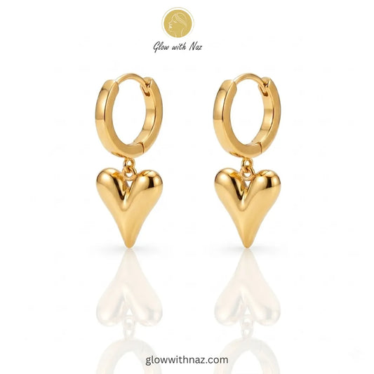Close-up view of polished gold-tone heart drop earrings on a white background