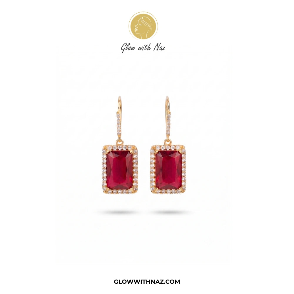 A pair of gold drop earrings featuring rectangular emerald-cut deep red ruby centers, surrounded by a halo of small clear pavé stones, shown on a white background with the brand logo 'Glow with Naz' at the top. studs earrings, small earrings, girls earrings, simple earrings, earrings for girls, black earrings, earrings, ear rings, earrings tops, stud earrings, tops earrings, aesthetic earrings, hoop earrings, drop earrings, diamond earrings, pink earrings, green earrings, ear ring, earrings for women, flowe