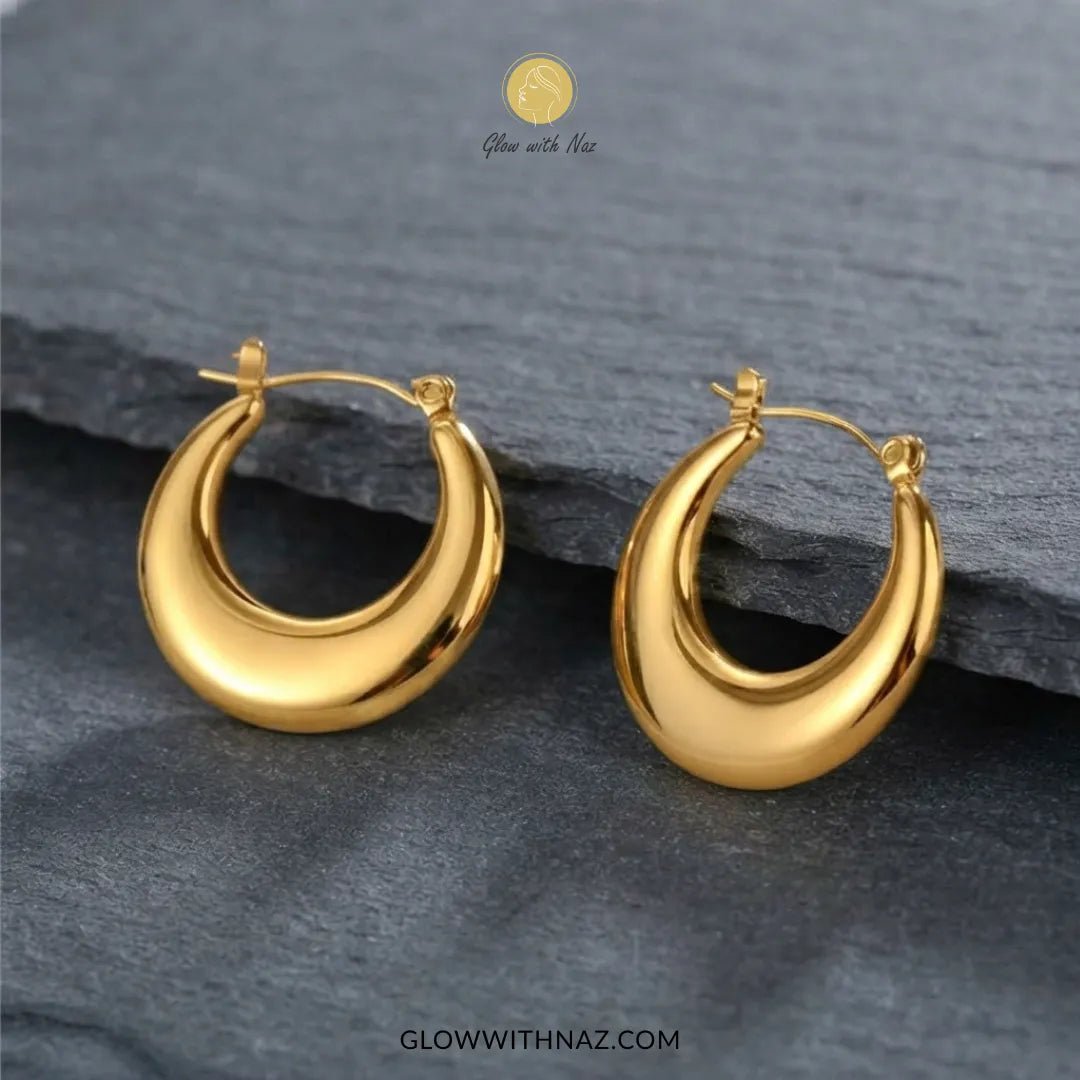 Gold Stainless Steel Plain Thick Chunky Baali Hoop Earrings - #Gold Stainless Steel Plain Thick Chunky Baali Hoop EarringsJewelryGlow With NazGlow With NazE0100A pair of polished gold crescent-shaped hoop earrings displayed on a dark slate surface. The brand logo 'Glow with Naz' is visible at the top, and the website 'GLOWWITHNAZ.#