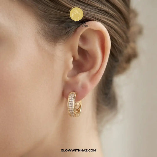 Golden Zircon Mid Size Slide Hoop for Women - Golden Zircon Mid Size Slide Hoop for WomenJewelryGlow With NazGlow With NazE058A close-up of a model's ear wearing a small gold hoop earring set with clear stones. The image features a brand watermark 'Glow With Naz' and a website URL at the bottom.