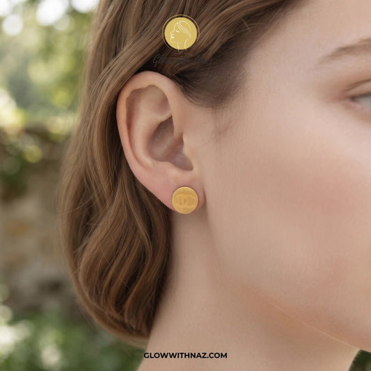 Minimal Stainless Steel Channel Coin Stud Earring - Minimal Stainless Steel Channel Coin Stud EarringJewelryGlow With NazGlow With NazE043A close-up of a woman's ear wearing a small round gold stud earring, with a matching gold hair clip visible in her hair. The background is softly blurred outdoor greenery. studs earrings, small earrings, girls earrings, simple earrings, earrings for girls, black earrings, earrings, ear rings, earrings tops, stud earrings, tops earrings, aesthetic earrings, hoo