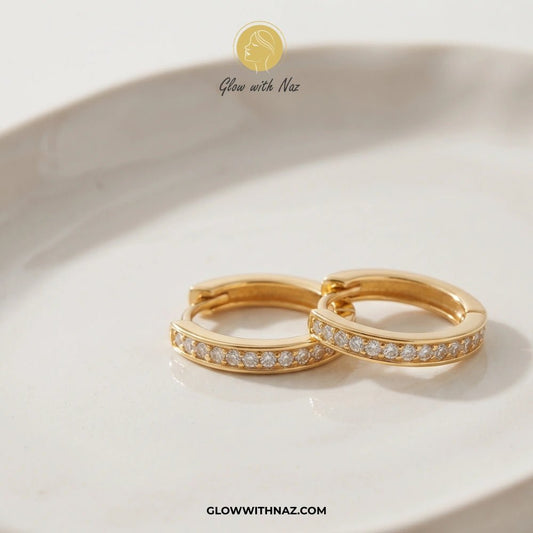 Premium Gold Plated Glass Crystal Hoops for Women - Premium Gold Plated Glass Crystal Hoops for WomenJewelryGlow With NazGlow With NazE040A pair of gold huggie hoop earrings with a row of small clear pavé stones, resting on a white ceramic dish. The brand logo 'Glow with Naz' is visible at the top, and the website 'GLOWWITHNAZ. studs earrings, small earrings, girls earrings, simple earrings, earrings for girls, black earrings, earrings, ear rings, earrings tops, stud earrings, tops earrings, aes