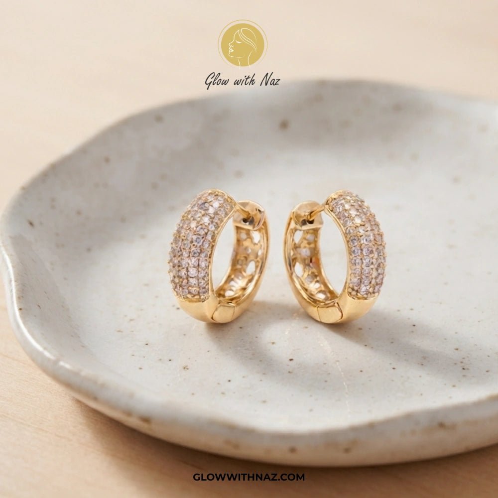Premium Statement Zircon Crystal Hoop Earrings for Women - Premium Statement Zircon Crystal Hoop Earrings for WomenJewelryGlow With NazGlow With NazE031A pair of gold huggie hoop earrings paved with small clear stones, displayed on a speckled ceramic dish. The brand logo 'Glow with Naz' is visible at the top and the website 'GLOWWITHNAZ.