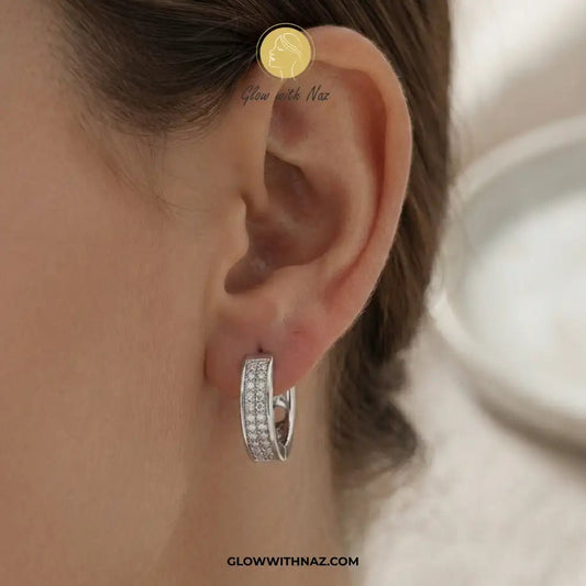 Silver Zircon Mid-Size Slide Hoop Earrings for Women - Silver Zircon Mid-Size Slide Hoop Earrings for WomenJewelryGlow With NazGlow With NazE059A close-up of a person's ear wearing a small silver hoop earring set with clear stones. The image includes a circular gold logo overlay reading 'Glow with Naz' and a website watermark at the bottom.