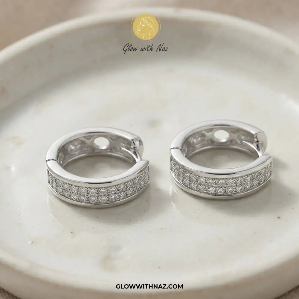 Silver Zircon Mid-Size Slide Hoop Earrings for Women - Silver Zircon Mid-Size Slide Hoop Earrings for WomenJewelryGlow With NazGlow With NazE059A pair of silver huggie hoop earrings with pavé-set clear stones, displayed on a light beige marble dish. The brand logo 'Glow with Naz' is visible at the top and the website 'GLOWWITHNAZ.