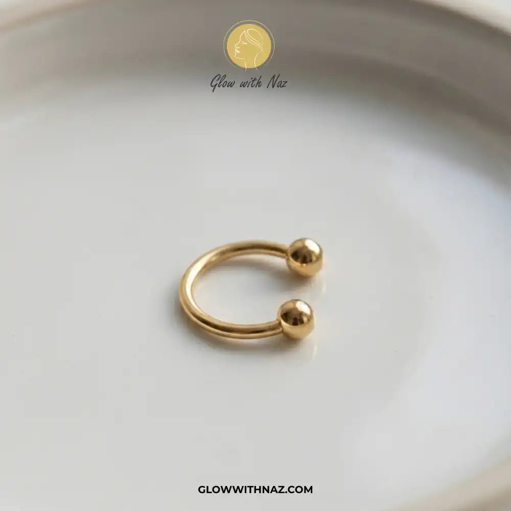 Stainless Steel Horseshoe 8.5 mm C Nose Ring & Helix Ear Piercing Jewelry - Stainless Steel Horseshoe 8.5 mm C Nose Ring & Helix Ear Piercing JewelryJewelryGlow With NazGlow With NazNR004A small gold open hoop ring with two polished ball ends, photographed on a white ceramic dish. The brand name Glow with Naz is visible as a watermark at the top, and the website GLOWWITHNAZ. nose ring, helix piercing jewelry, cartilage earring, horseshoe piercing, septum ring, stainless steel jewelry, body jewel