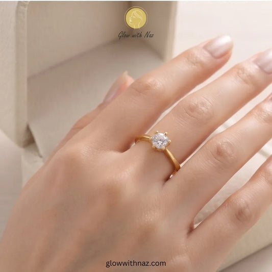 The Signature Adjustable 6-Grip Diamond Solitaire Ring - The Signature Adjustable 6-Grip Diamond Solitaire RingJewelryGlow With NazGlow With NazR024A close-up of a hand wearing a yellow gold ring with a single round-cut clear gemstone. The background shows a soft beige jewelry box, with the brand name 'Glow with Naz' ring, girls rings, rings for girls, rings simple, simple rings, stainless steel jewelry, jewellery set, aesthetic jewelry, simple jewellery, chain, jewelry, artificial jewelleryvisi