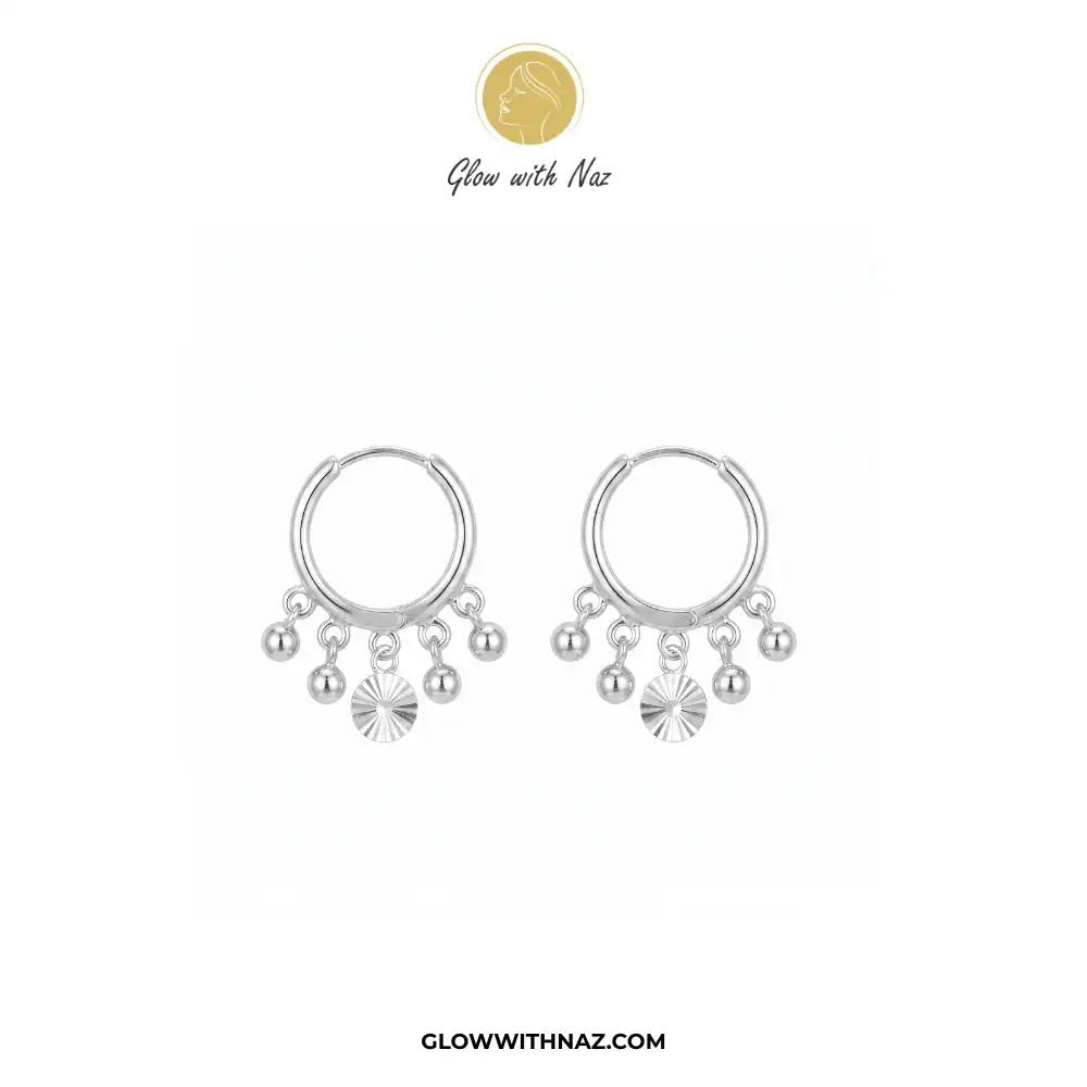 12mm Anti-Tarnish Silver 5 Drop Trending Hoops Earrings - 12mm Anti-Tarnish Silver 5 Drop Trending Hoops EarringsJewelryGlow With NazGlow With NazE045A pair of silver hoop earrings with dangling charms, including small beads and a sunburst disc, displayed on a white background with the brand logo 'Glow with Naz' at the top. Silver 3 Drop Separate Hoops, Glow With Naz earrings, stainless steel silver earrings, viral trending earrings, drop huggie hoops, silver dangle earrings, eye-catching drop h