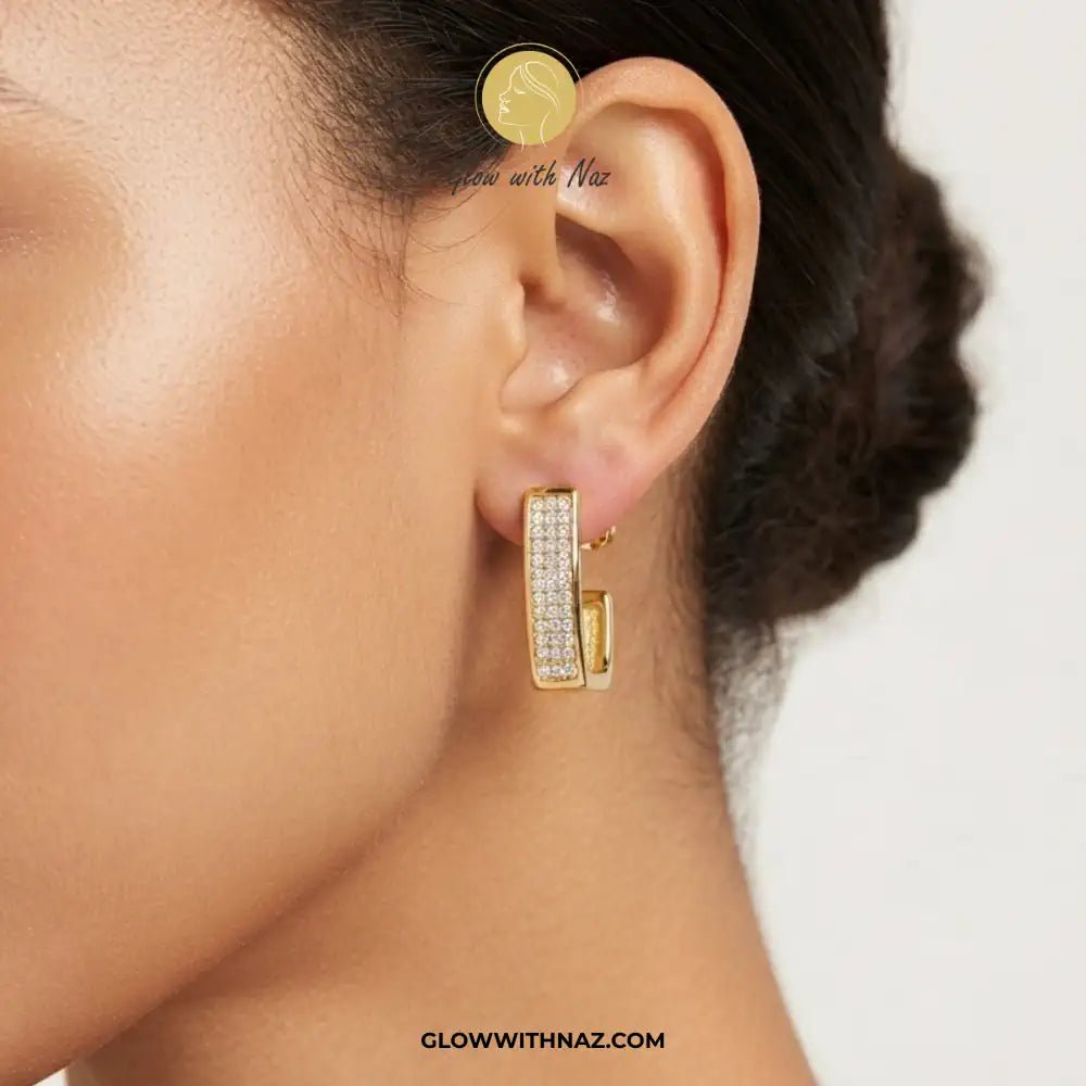 18K Gold Plated Diamond Square Geometric Statement Earrings - 18K Gold Plated Diamond Square Geometric Statement EarringsJewelryGlow With NazGlow With NazE053A close-up of a model's ear wearing a gold huggie hoop earring paved with small clear stones, with brand text 'Glow with Naz' and 'GLOWWITHAZ.COM' visible on the image.