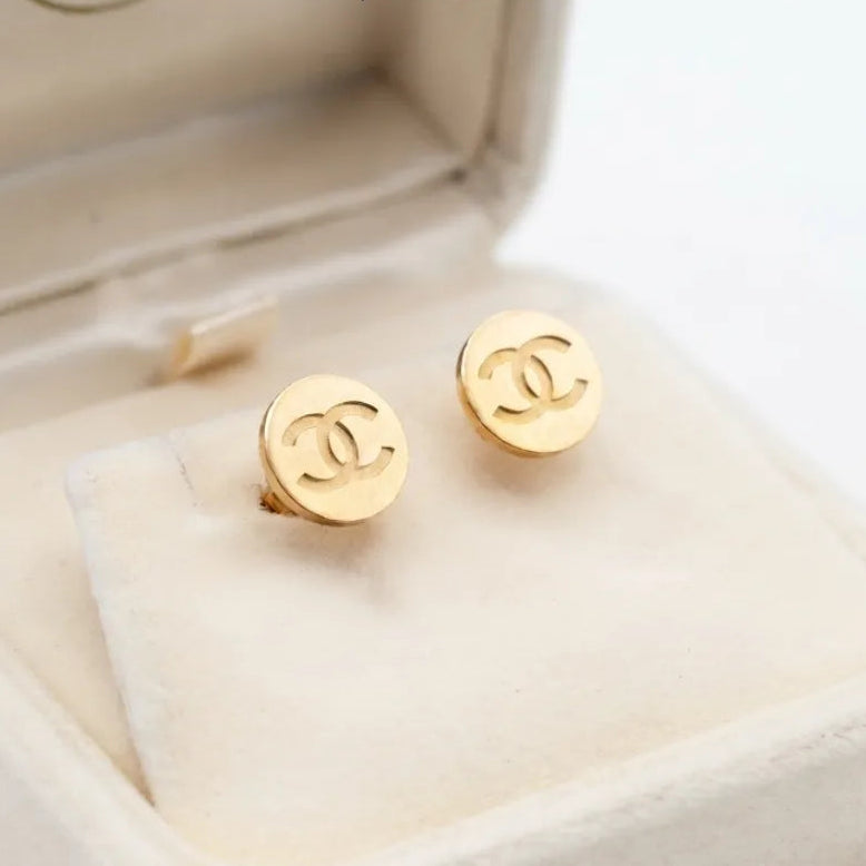 Minimal Stainless Steel Channel Coin Stud Earring - Minimal Stainless Steel Channel Coin Stud EarringJewelryGlow With NazGlow With NazE043A pair of round gold-tone Chanel stud earrings with the interlocking CC logo embossed on the front, displayed on a clean white background with Glow with Naz branding. studs earrings, small earrings, girls earrings, simple earrings, earrings for girls, black earrings, earrings, ear rings, earrings tops, stud earrings, tops earrings, aesthetic earrings, hoop ear