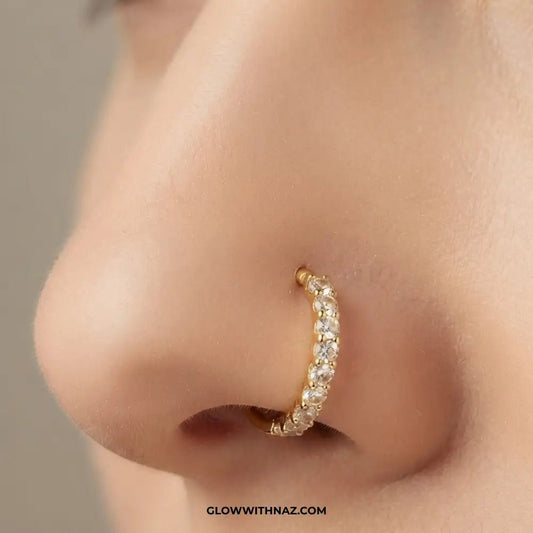 7.5 mm Outer Zircon Stainless Steel Nose Ring - 7.5 mm Outer Zircon Stainless Steel Nose RingJewelryGlow With NazGlow With NazNR005A close-up of a person's nose wearing a small gold crescent huggie hoop earring adorned with clear pavé stones. The image features a watermark at the bottom reading 'GLOWWITHNAZ. nose ring, front zircon nose ring, stainless steel nose ring, zircon nose ring, gold nose ring, silver nose ring, hoop nose ring, septum ring, cartilage earring, helix piercing, tragus jewel