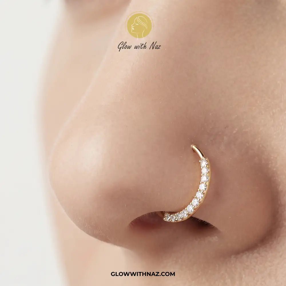 9 mm Anti Tarnish Front Zircon Stainless Steel Nose Ring - 9 mm Anti Tarnish Front Zircon Stainless Steel Nose RingJewelryGlow With NazGlow With NazNR006A close-up of a person's nose wearing a gold crescent-shaped nose hoop adorned with small clear stones. The brand name 'Glow with Naz' is visible as an overlay. nose ring, front zircon nose ring, stainless steel nose ring, zircon nose ring, gold nose ring, silver nose ring, hoop nose ring, septum ring, cartilage earring, helix piercing, tragus j