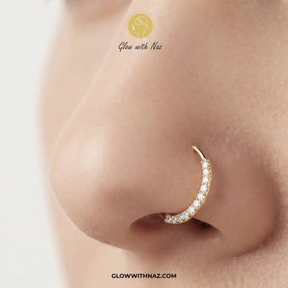 9 mm Anti Tarnish Front Zircon Stainless Steel Nose Ring - 9 mm Anti Tarnish Front Zircon Stainless Steel Nose RingJewelryGlow With NazGlow With NazNR006A close-up of a person's nose wearing a gold crescent-shaped nose hoop adorned with small clear stones. The brand name 'Glow with Naz' is visible as an overlay. nose ring, front zircon nose ring, stainless steel nose ring, zircon nose ring, gold nose ring, silver nose ring, hoop nose ring, septum ring, cartilage earring, helix piercing, tragus j