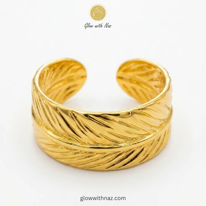 Close-up of a high-polished stainless steel gold ring with an artistic, wrap-around feather motif.