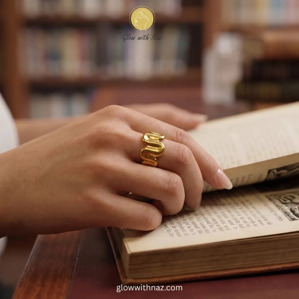 Close-up of a high-shine, gold-plated stainless steel ring with an artistic molten wave shape.