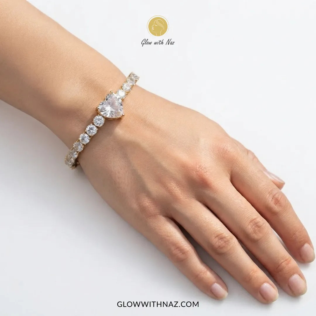 A close-up of a person's hand and wrist wearing a delicate bracelet with a large pear-cut clear center stone and smaller clear stones along the band. The image has Glow with Naz branding on a clean white background.