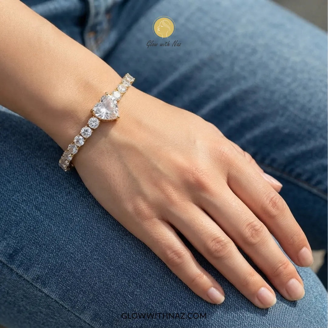 A close-up of a person's hand and wrist wearing a gold-toned bracelet adorned with clear stones, resting on blue denim jeans. The brand name Glow with Naz is visible as an overlay.