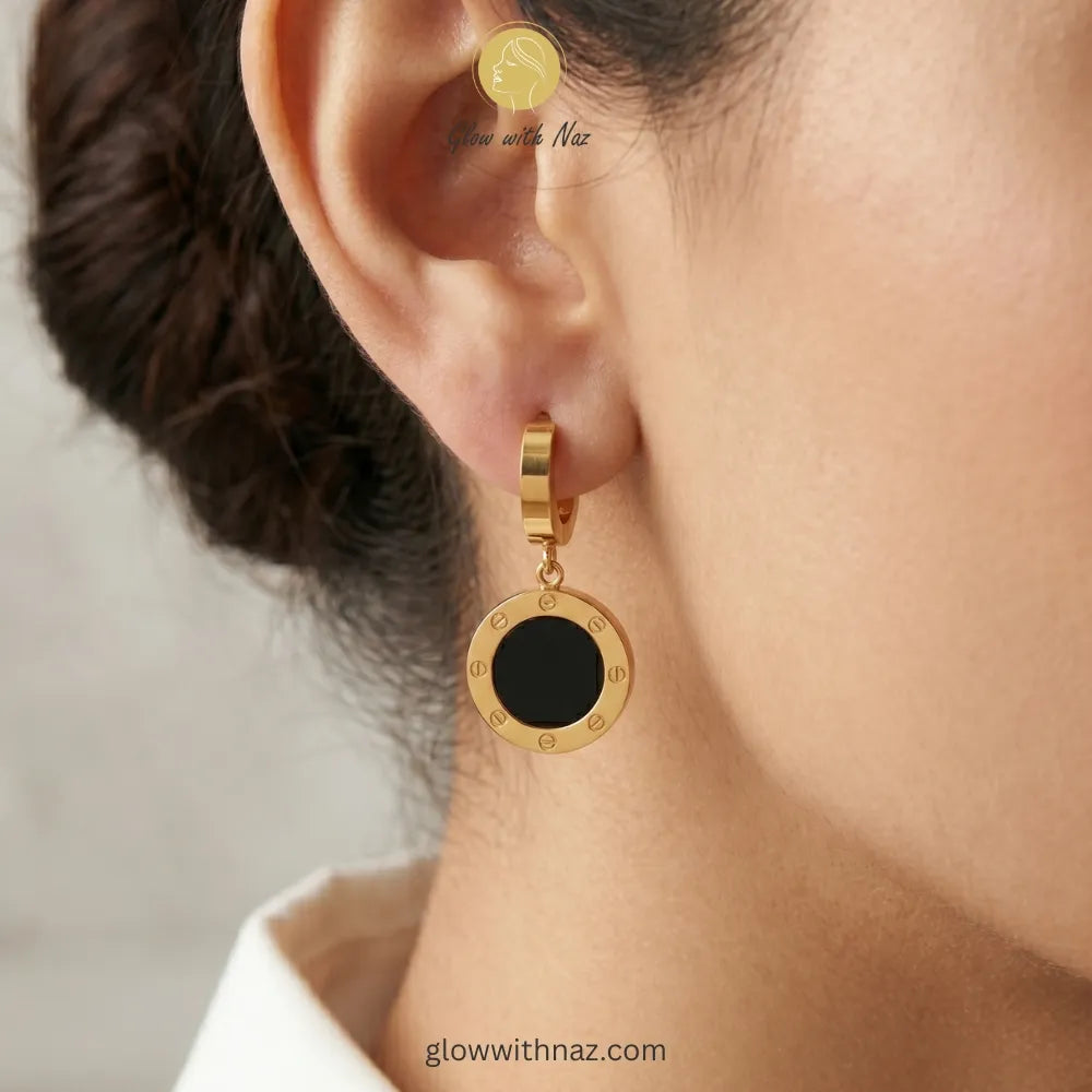 Close-up view of polished black and gold circular drop earrings on a white background