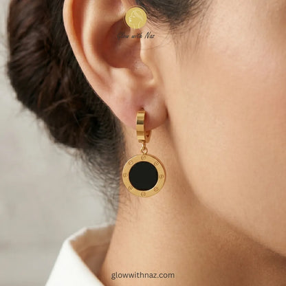 Close-up view of polished black and gold circular drop earrings on a white background
