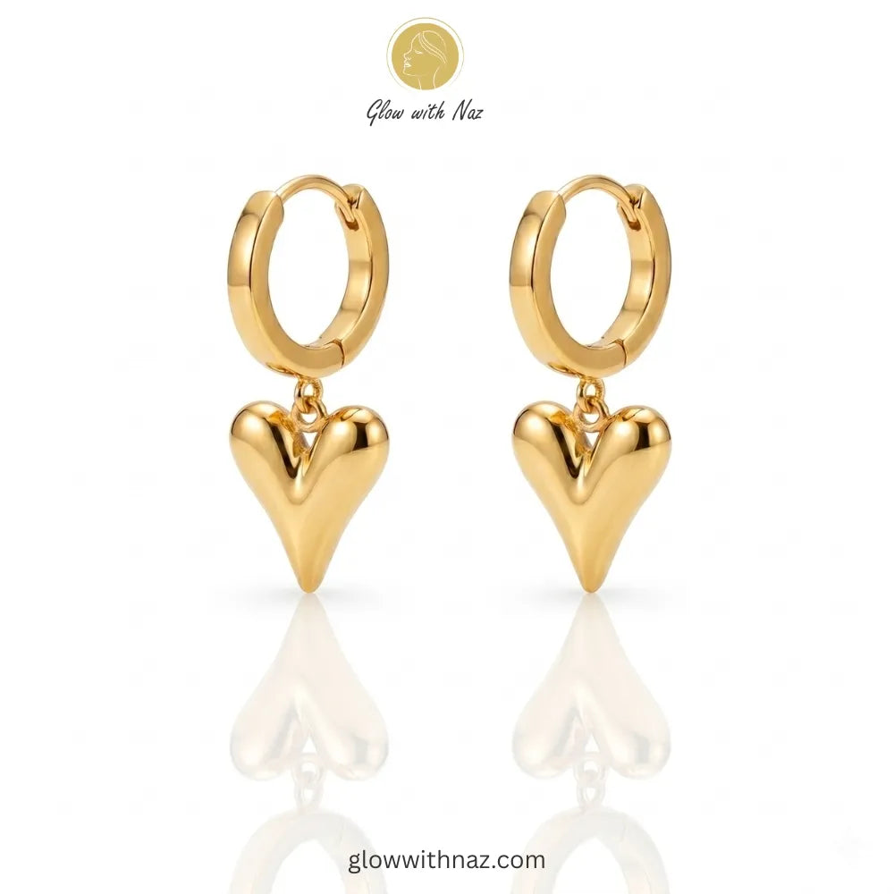 Close-up view of polished gold-tone heart drop earrings on a white background