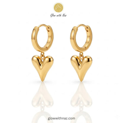 Close-up view of polished gold-tone heart drop earrings on a white background