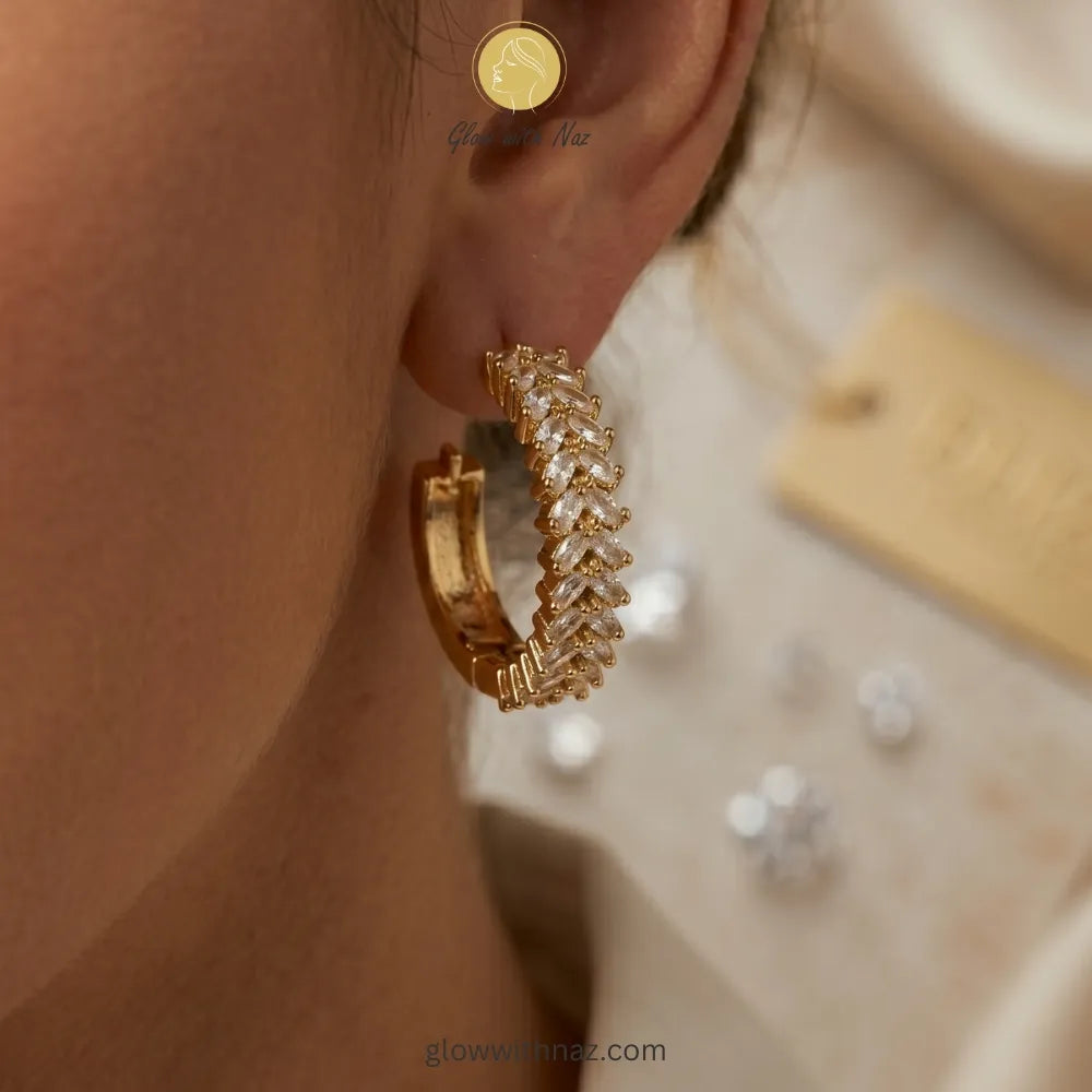Close-up view of sparkling gold marquise-cut crystal hoop earrings on a white background
