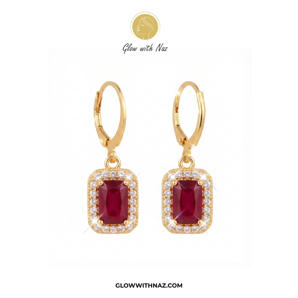 A pair of gold leverback drop earrings featuring rectangular emerald-cut red gemstones surrounded by small clear stones, displayed on a white background with the brand name Glow with Naz. 