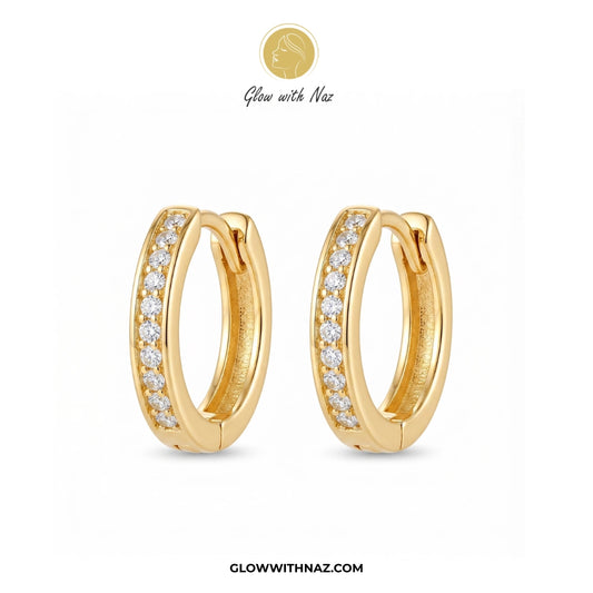 A pair of gold huggie hoop earrings with a row of clear pavé stones on the front, displayed on a clean white background with the brand logo 'Glow with Naz' at the top and the website 'GLOWWITHNAZ.COM' at the bottom. studs earrings, small earrings, girls earrings, simple earrings, earrings for girls, black earrings, earrings, ear rings, earrings tops, stud earrings, tops earrings, aesthetic earrings, hoop earrings, drop earrings, diamond earrings, pink earrings, green earrings, ear ring, earrings for women, 