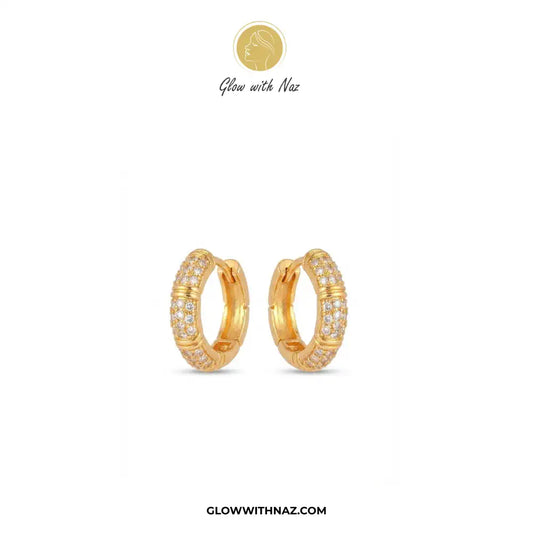 A pair of gold huggie hoop earrings with pavé-set clear stones, displayed on a clean white background with the brand logo 'Glow with Naz' at the top and the website 'GLOWWITHNAZ.COM' at the bottom.