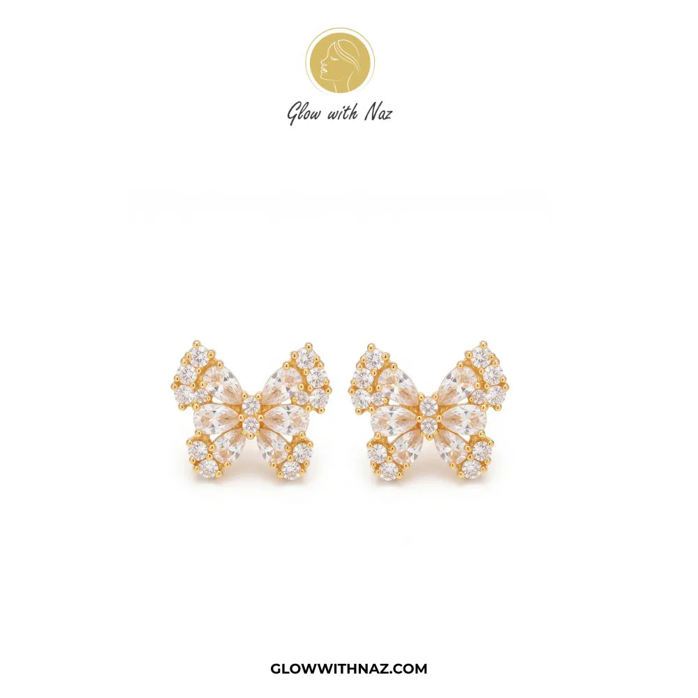 A pair of gold butterfly-shaped stud earrings adorned with clear crystals, displayed on a clean white background with the brand logo 'Glow with Naz' at the top and 'GLOWWITHNAZ.COM' at the bottom.