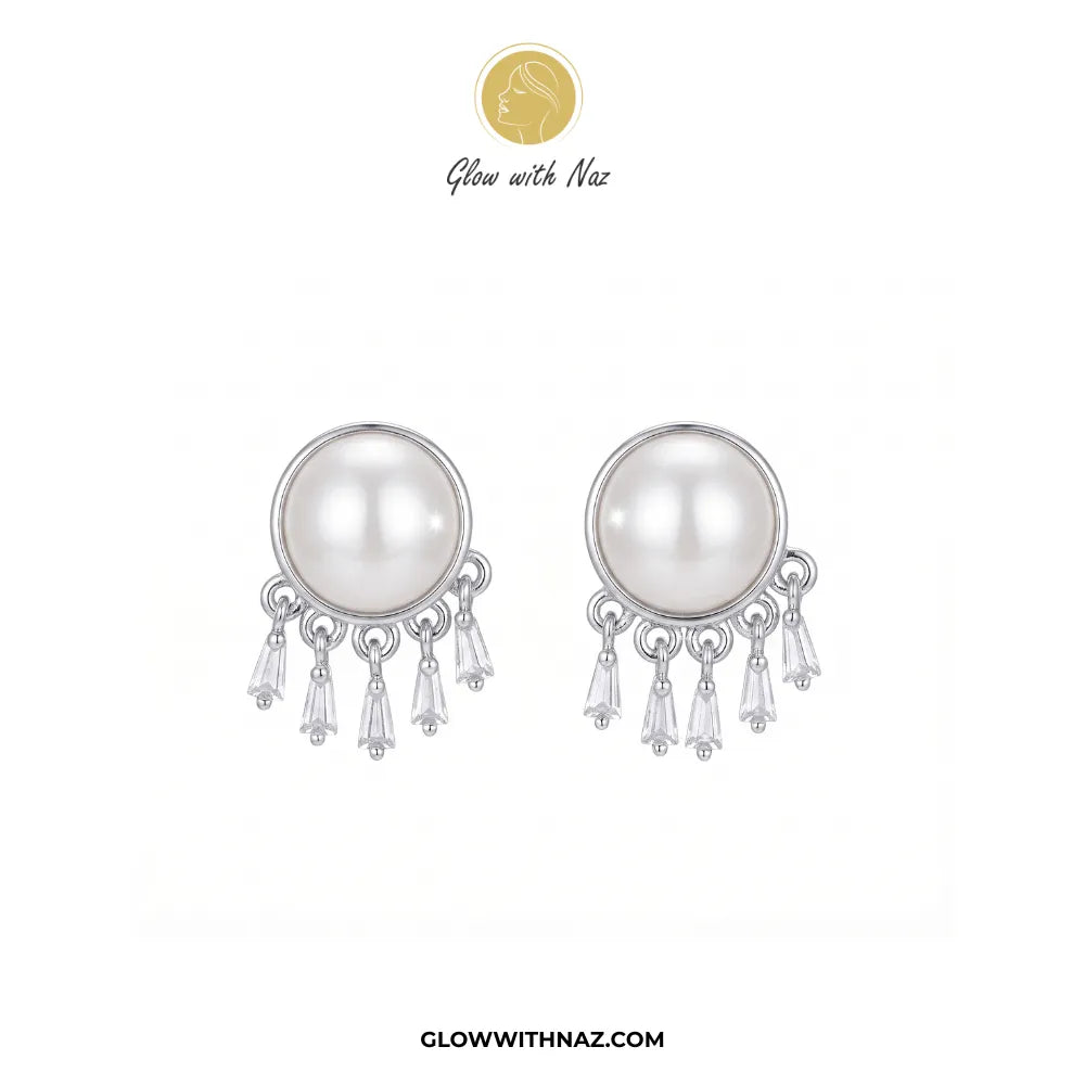 A pair of silver-toned dangle earrings featuring a large white pearl in a round bezel setting, with three clear crystal drops hanging below. The brand logo 'Glow with Naz' is displayed at the top, and the website 'GLOWWITHNAZ.