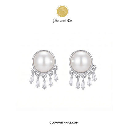 A pair of silver-toned dangle earrings featuring a large white pearl in a round bezel setting, with three clear crystal drops hanging below. The brand logo 'Glow with Naz' is displayed at the top, and the website 'GLOWWITHNAZ.