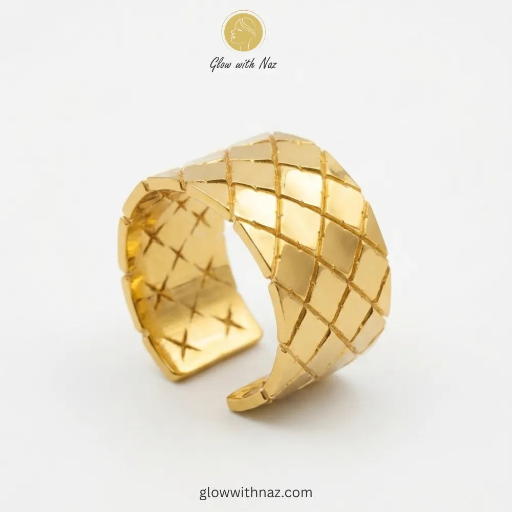A wide-band gold ring featuring a textured quilted diamond pattern with an adjustable cuff design.