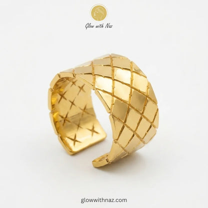 A wide-band gold ring featuring a textured quilted diamond pattern with an adjustable cuff design.