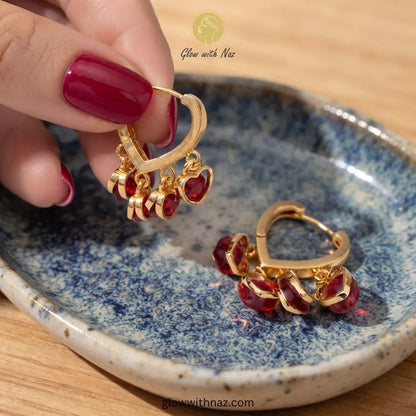 Gold plated heart hoop earrings featuring four dangling ruby red heart cubic zirconia crystal charms by Glow With Naz