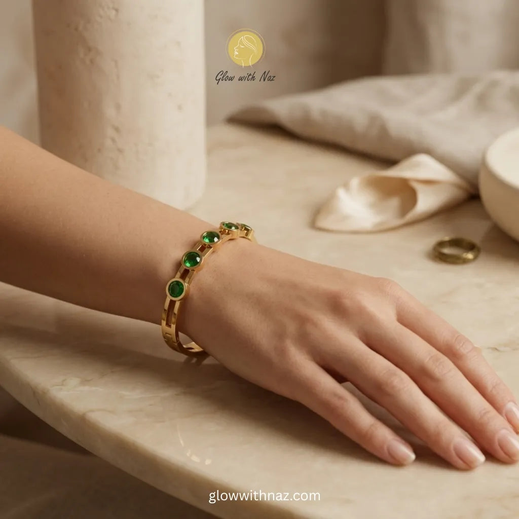 Woman wearing gold bangle with green stones on wrist, elegant style
