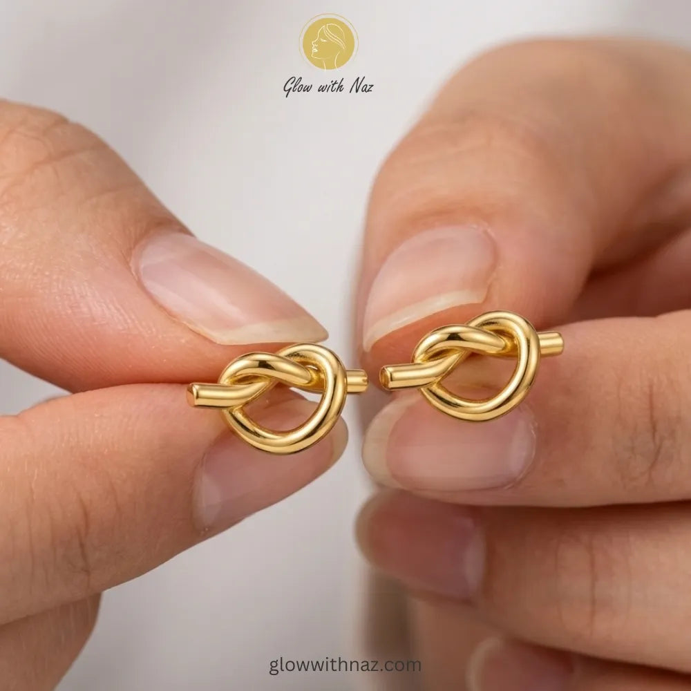 Minimalist gold-tone knot stud earrings being held, showcasing polished finish