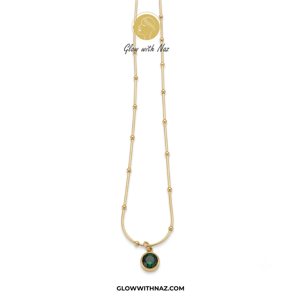 Gold necklace with a green pendant on a white background, branded 'Glow with Naz'. necklace, pendant necklace, necklace set, locket set, simple necklace, pendant set, pendant, chain necklace, diamond pendant, diamond necklace, locket necklace, neck chain, girls locket, heart locket, pendant for girls, necklace for girls, heart necklace, locket for girls, diamond locket, pendant necklace for girls, heart chain locket, stainless steel necklace, double chain necklace, ruby necklace, neck chain for girls, locke