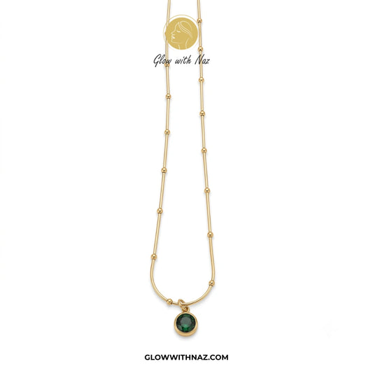 Gold necklace with a green pendant on a white background, branded 'Glow with Naz'. necklace, pendant necklace, necklace set, locket set, simple necklace, pendant set, pendant, chain necklace, diamond pendant, diamond necklace, locket necklace, neck chain, girls locket, heart locket, pendant for girls, necklace for girls, heart necklace, locket for girls, diamond locket, pendant necklace for girls, heart chain locket, stainless steel necklace, double chain necklace, ruby necklace, neck chain for girls, locke