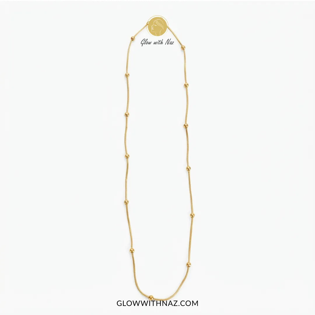 A gold chain necklace with small bead accents and a round medallion pendant, shown on a plain white background. The text 'Glow with Naz' appears near the top of the necklace, and 'GLOWWITHNAZ.