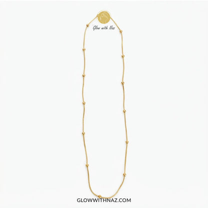 A gold chain necklace with small bead accents and a round medallion pendant, shown on a plain white background. The text 'Glow with Naz' appears near the top of the necklace, and 'GLOWWITHNAZ.