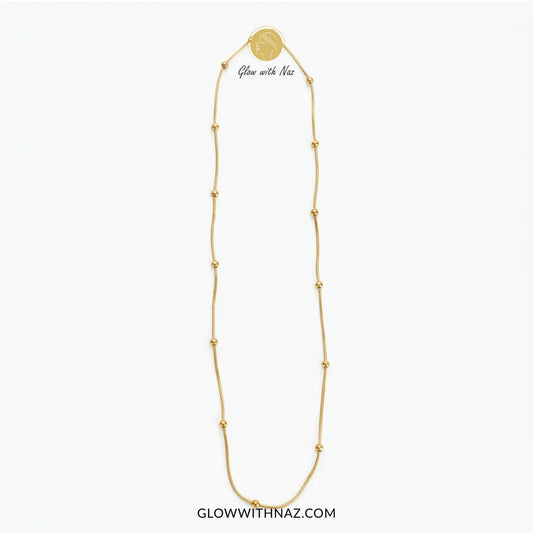 A gold chain necklace with small bead accents and a round medallion pendant, shown on a plain white background. The text 'Glow with Naz' appears near the top of the necklace, and 'GLOWWITHNAZ.