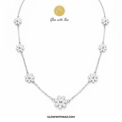 A silver floral necklace featuring five small daisy-like flower charms spaced along a delicate chain, displayed on a clean white background with the brand logo 'Glow with Naz' and website text.