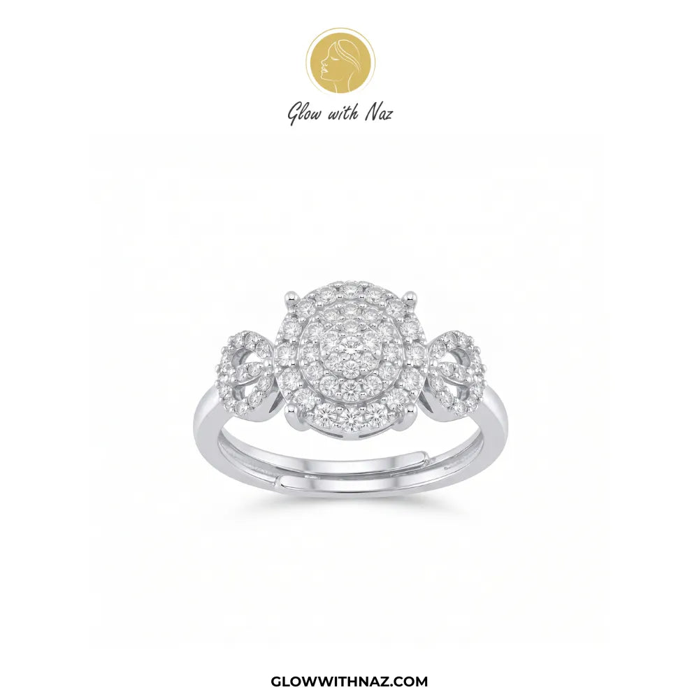 A three-stone diamond ring in a silver-colored metal setting, featuring a large central round diamond cluster flanked by two smaller round diamond clusters on a white background, with the Glow with Naz brand logo at the top.