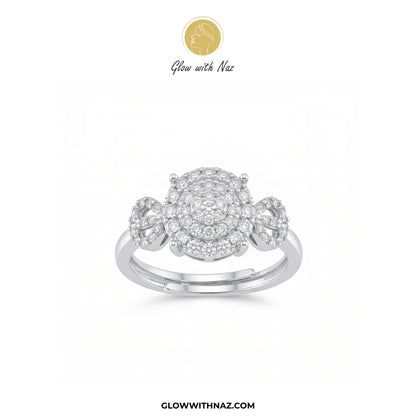 A three-stone diamond ring in a silver-colored metal setting, featuring a large central round diamond cluster flanked by two smaller round diamond clusters on a white background, with the Glow with Naz brand logo at the top.