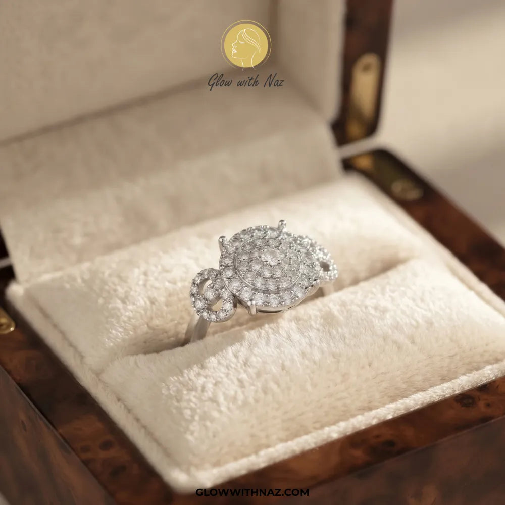 A silver-toned pavé ring with a floral or leaf-like cluster design, displayed in a cream velvet-lined jewelry box. The ring features clear stones set in a silver-colored metal.