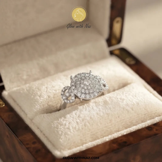 A silver-toned pavé ring with a floral or leaf-like cluster design, displayed in a cream velvet-lined jewelry box. The ring features clear stones set in a silver-colored metal.