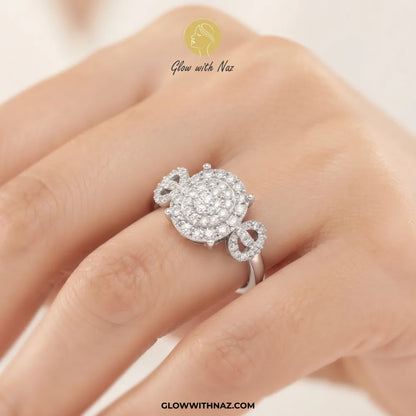 A silver ring with a pavé diamond cluster and bow details, shown worn on a hand. The brand logo 'Glow with Naz' is visible at the top and 'GLOWWITHNAZ.