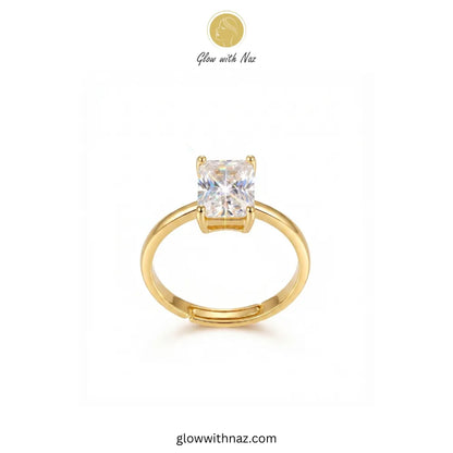 A gold solitaire ring with a square-cut clear gemstone, displayed on a clean white background with a brand logo 'Glow with Naz' at the top.